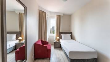 Ein Hotelzimmer mit Bett, Stuhl, Nachttisch und einem Fenster mit Vorhängen.