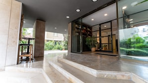 A hotel entrance with marble steps, a wooden stool, and a glass door leading to a room with a potted plant. - The Marmara Suadiye Residence (Istanbul)