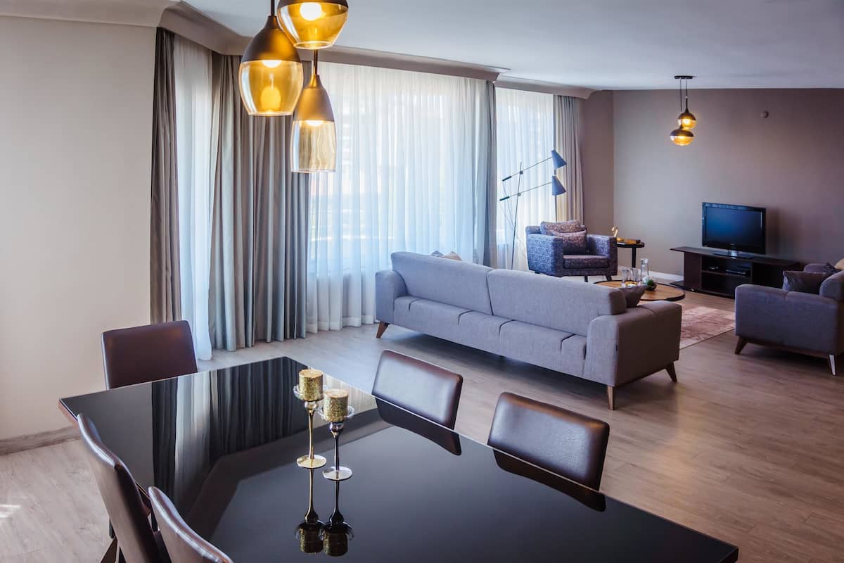 A modern living room with a sofa, a dining table with chairs, a TV, and a chandelier.
