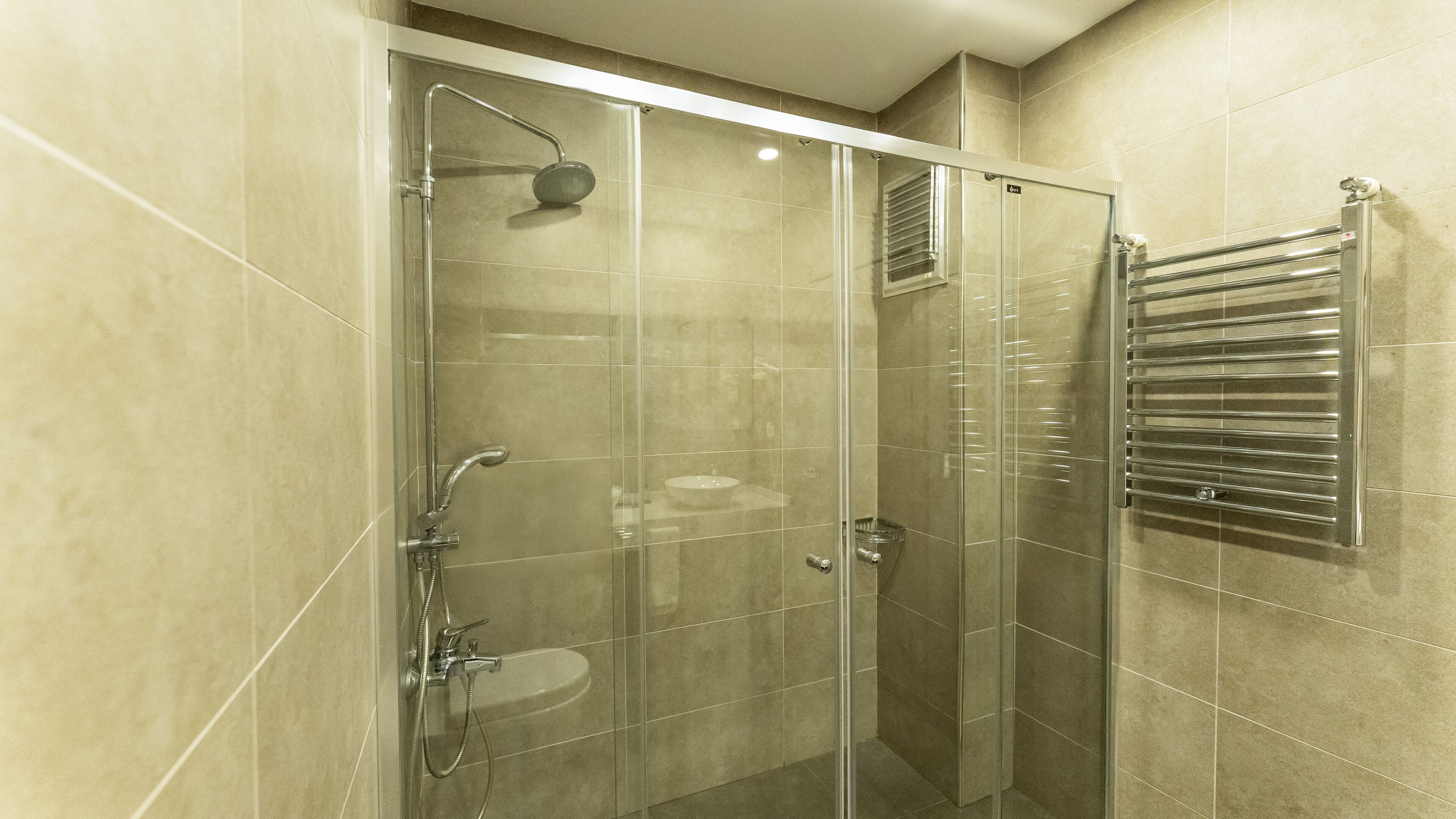 A glass-enclosed shower with a handheld showerhead and a handheld faucet.
