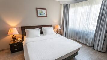 A neatly made bed with white linens, two bedside lamps, a nightstand with a telephone, and a framed picture on the wall.