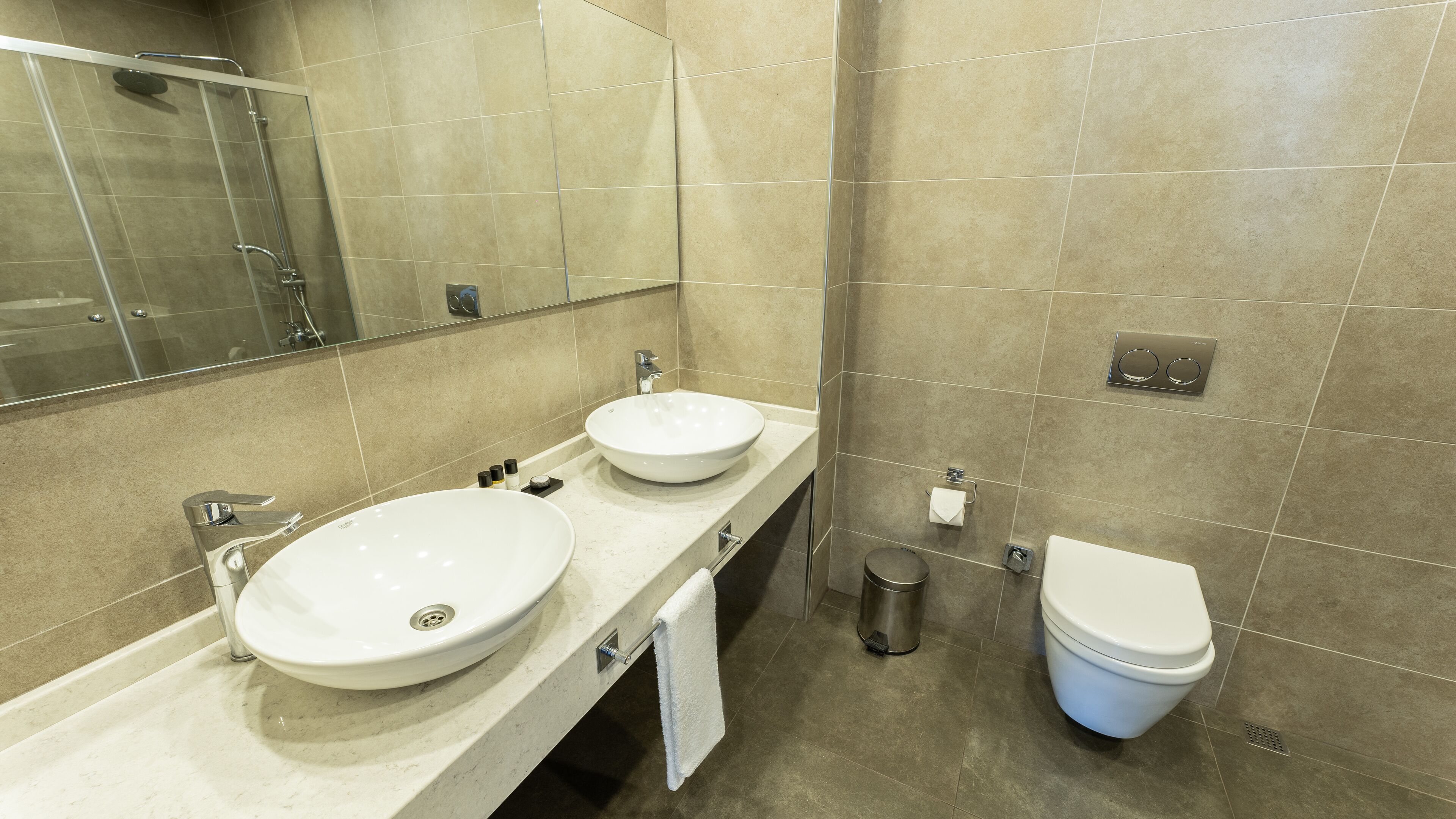 A modern bathroom with two sinks, a toilet, and a shower.