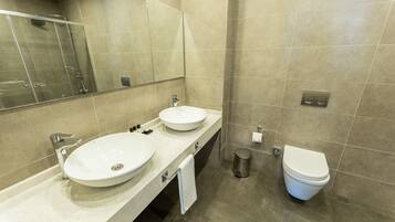 A modern bathroom with two sinks, a toilet, and a shower.