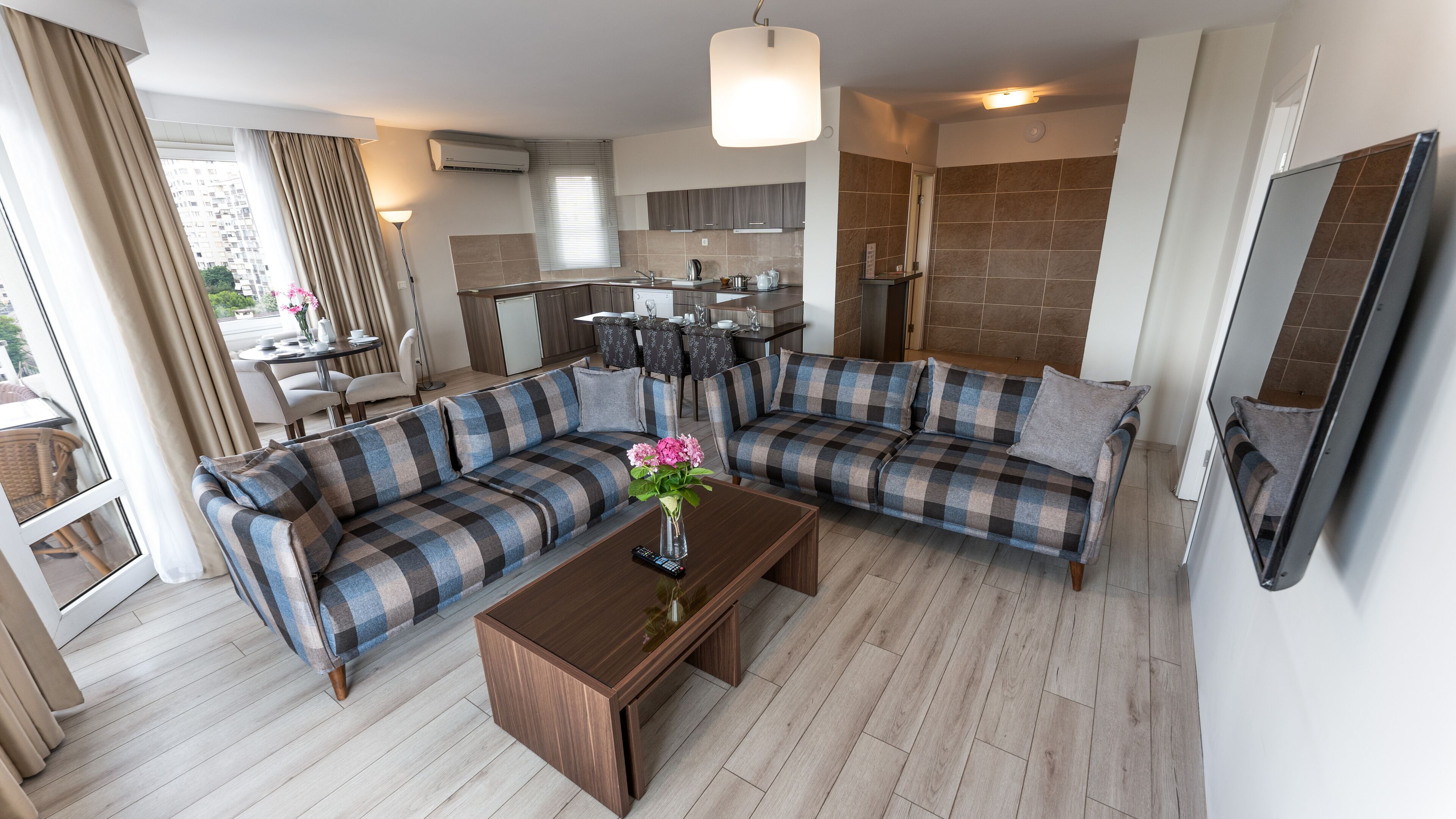 A modern living room with a checkered sofa, a coffee table, and a dining area with a kitchen in the background.
