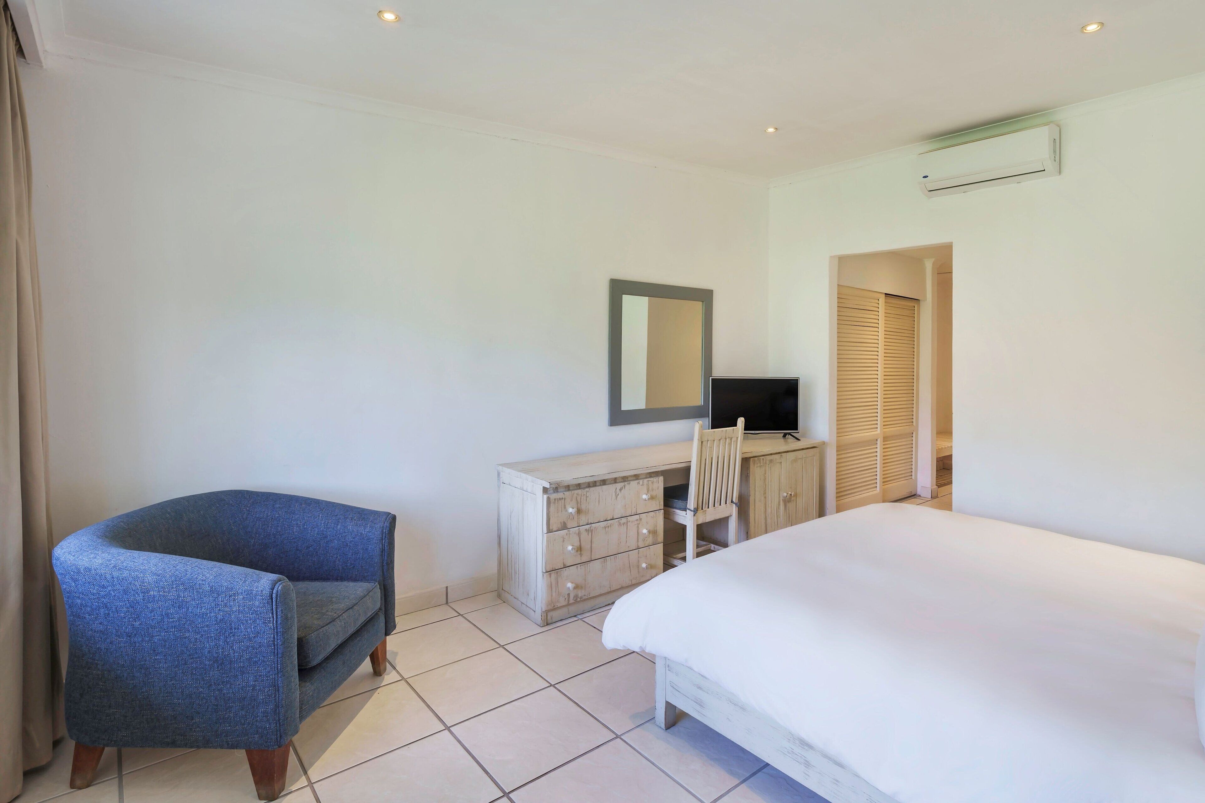 A bedroom with a bed, a desk with a chair, a dresser, a mirror, and a television.