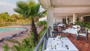 A poolside dining area with tables set for two, overlooking a swimming pool, surrounded by lush greenery and palm trees. - Protea Hotel by Marriott Chingola (Chingola)