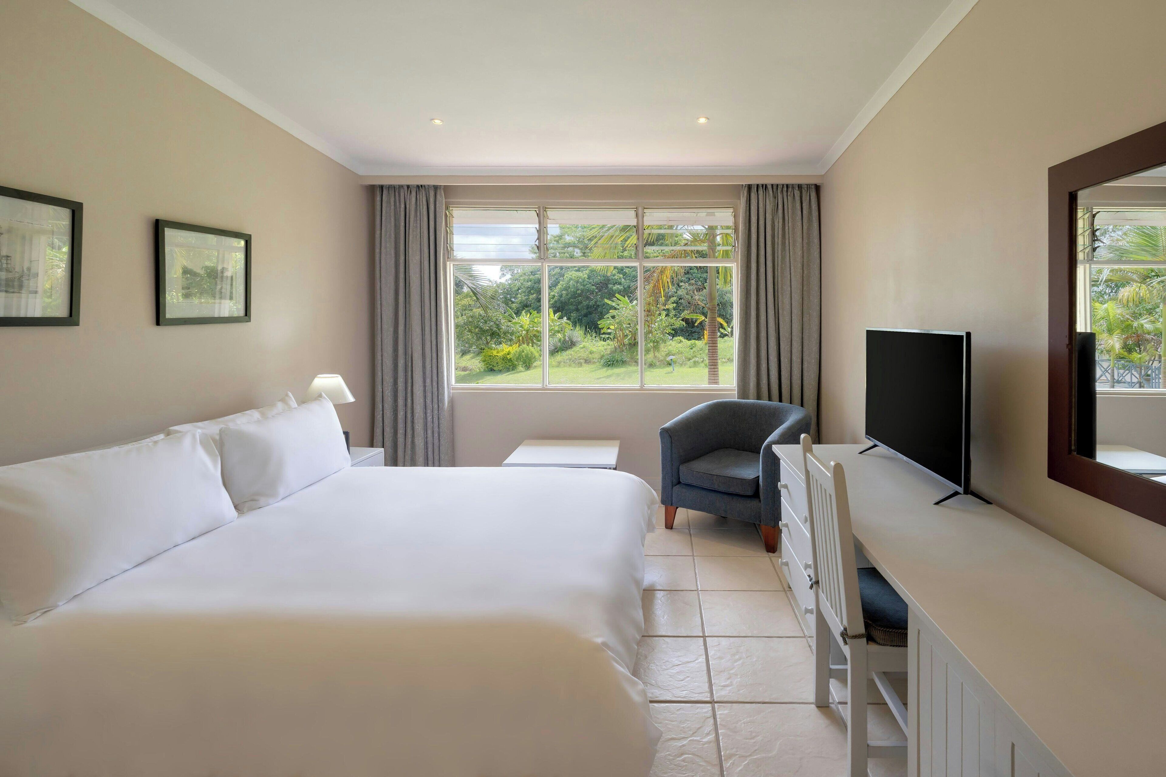 Habitación de hotel con una cama grande, un escritorio con televisor y una ventana con vistas a zonas verdes.