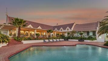 A hotel with a swimming pool, lounge chairs, and a covered patio area.