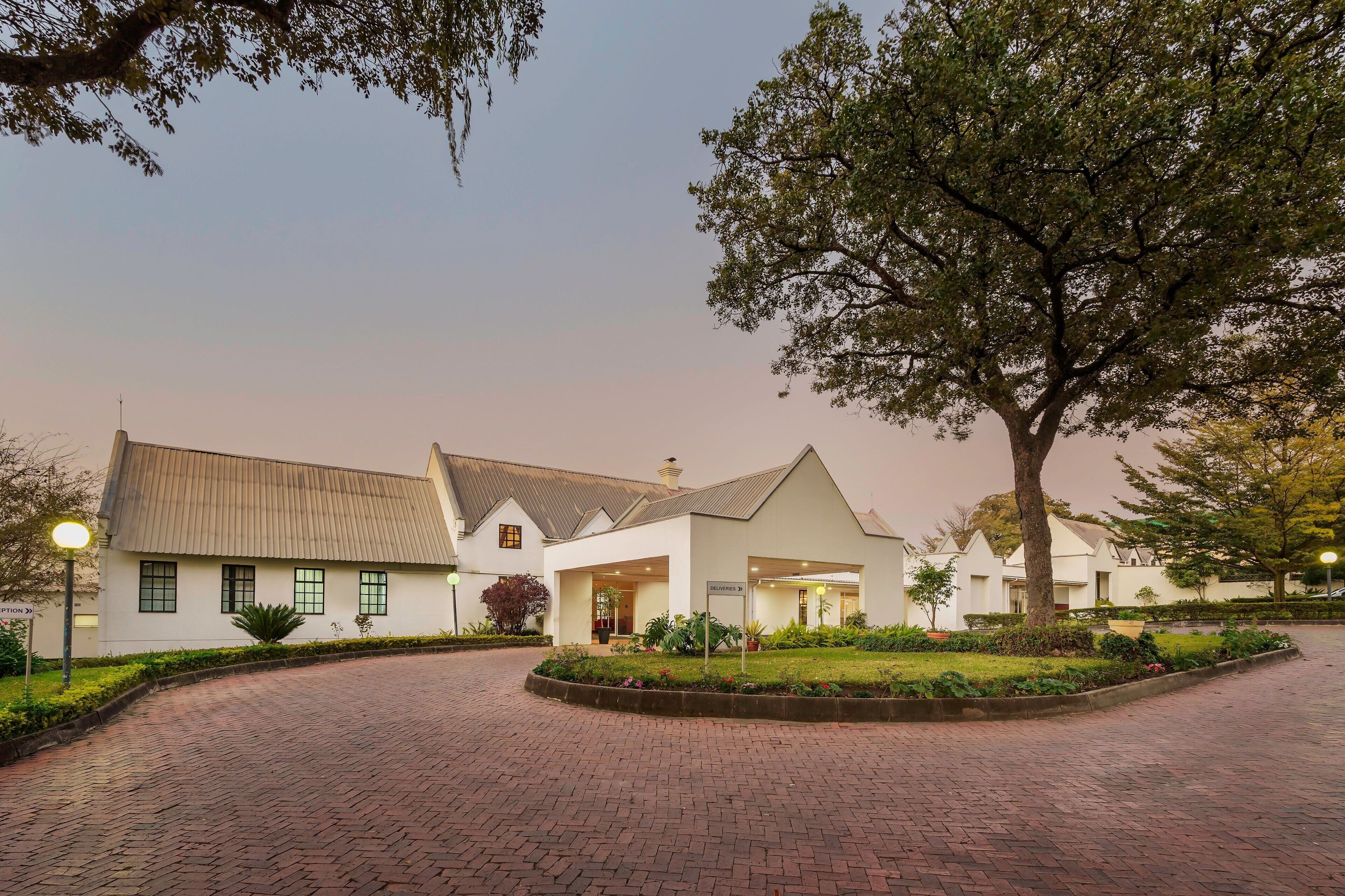 A building with a brick pathway leading to a gated entrance, surrounded by greenery and trees.