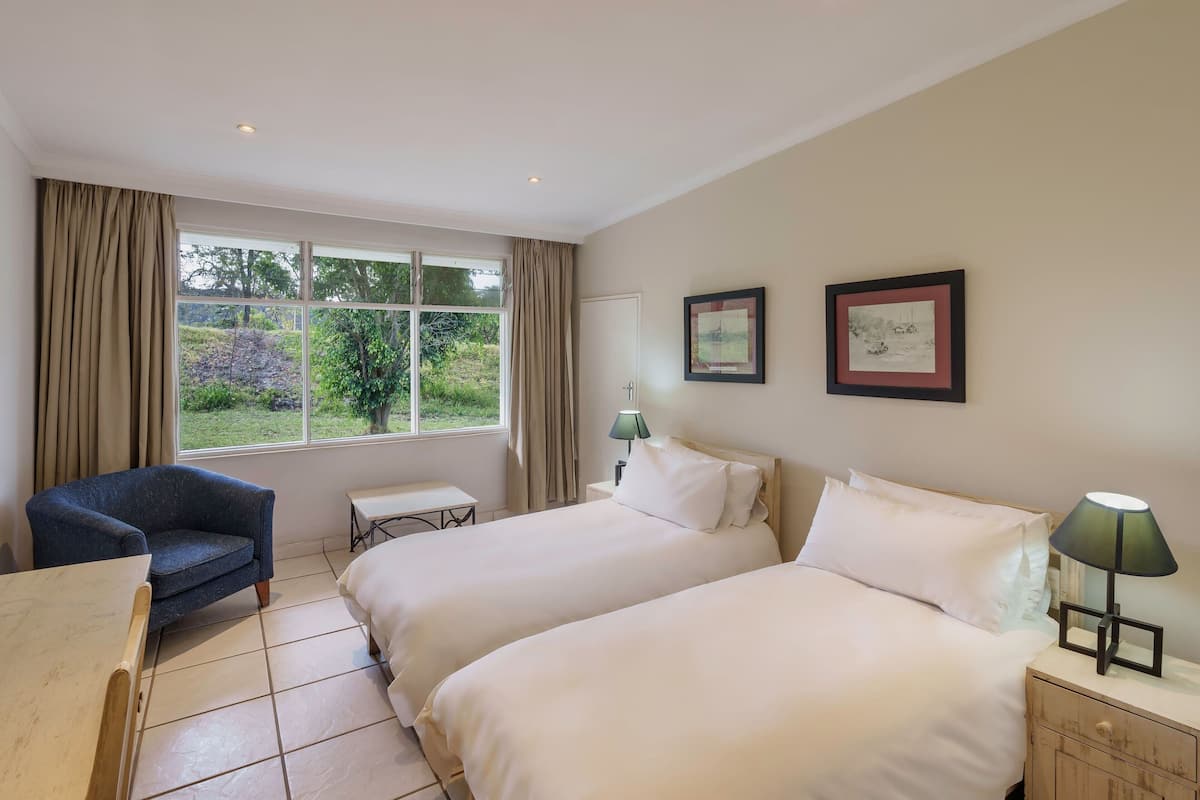 A hotel room with two beds, a desk, a chair, and a window with curtains.