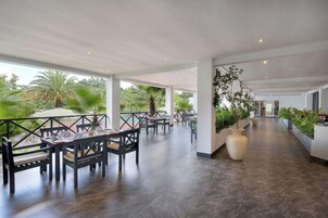 Un área de comedor al aire libre con mesas y sillas, rodeada de follaje y vistas a la piscina.