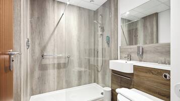 Un baño moderno con ducha a ras de suelo, bañera, inodoro y tocador con espejo.
