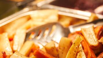 Primer plano de un bufé con diversos platos, que incluyen una mezcla de verduras y quizás algo de carne, servidos en una bandeja con un tenedor y una cuchara.