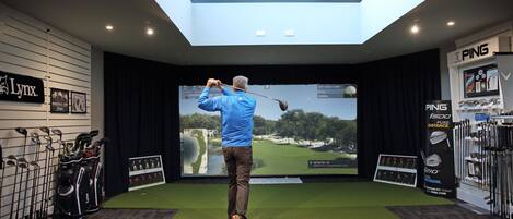 Une salle de simulation de golf équipée d’un grand écran, de sacs de golf et d’une lucarne au plafond.
