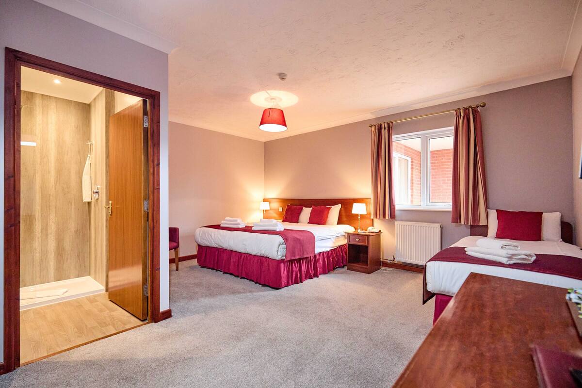 Une chambre d’hôtel avec deux lits, une porte en bois, une fenêtre avec des rideaux et un luminaire suspendu rouge.
