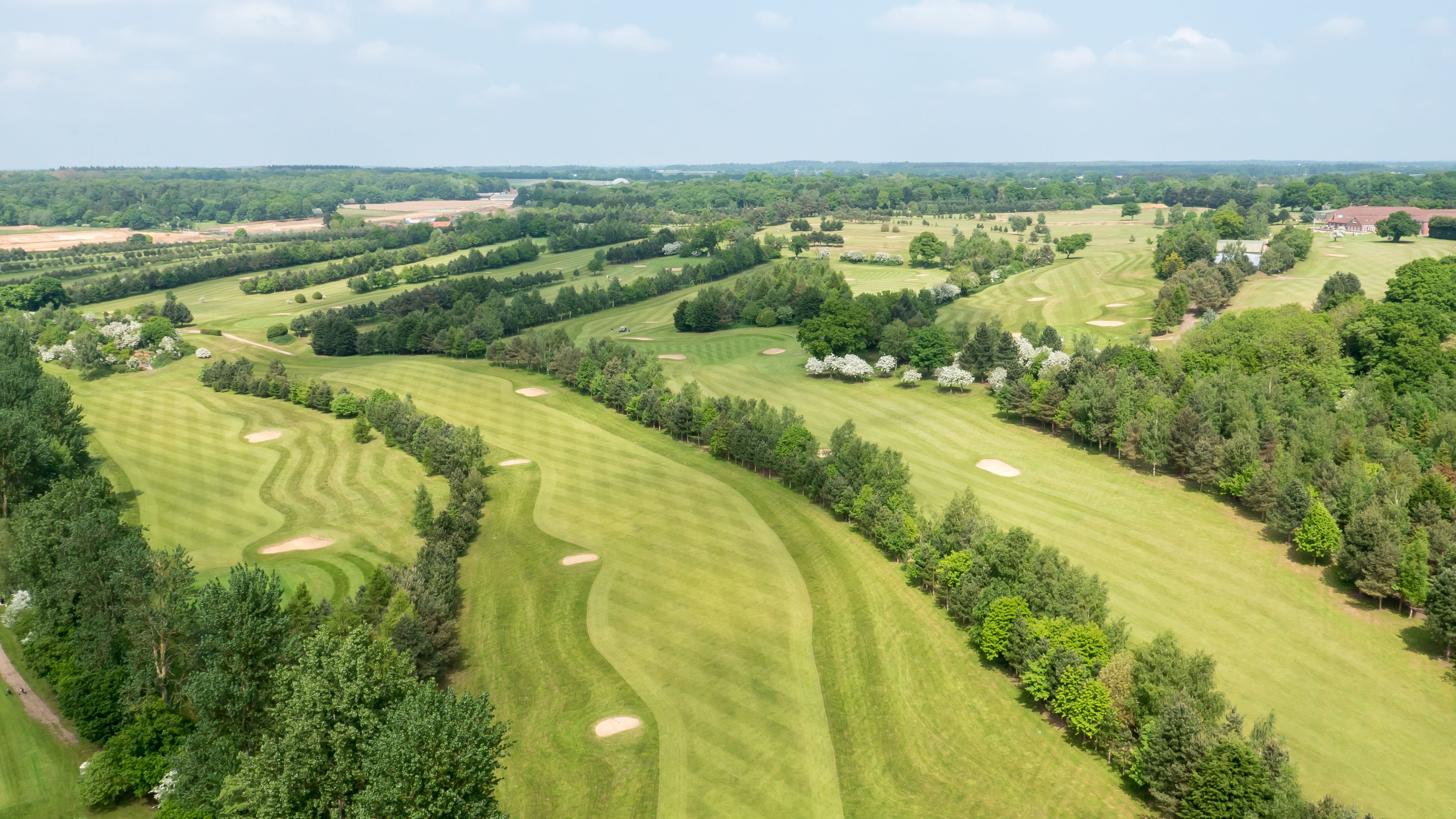 A golf course with well-maintained fairways, sand bunkers, and dense tree lines.