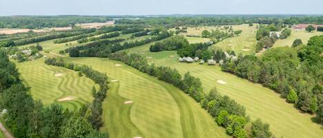 A golf course with well-maintained fairways, sand bunkers, and dense tree lines.