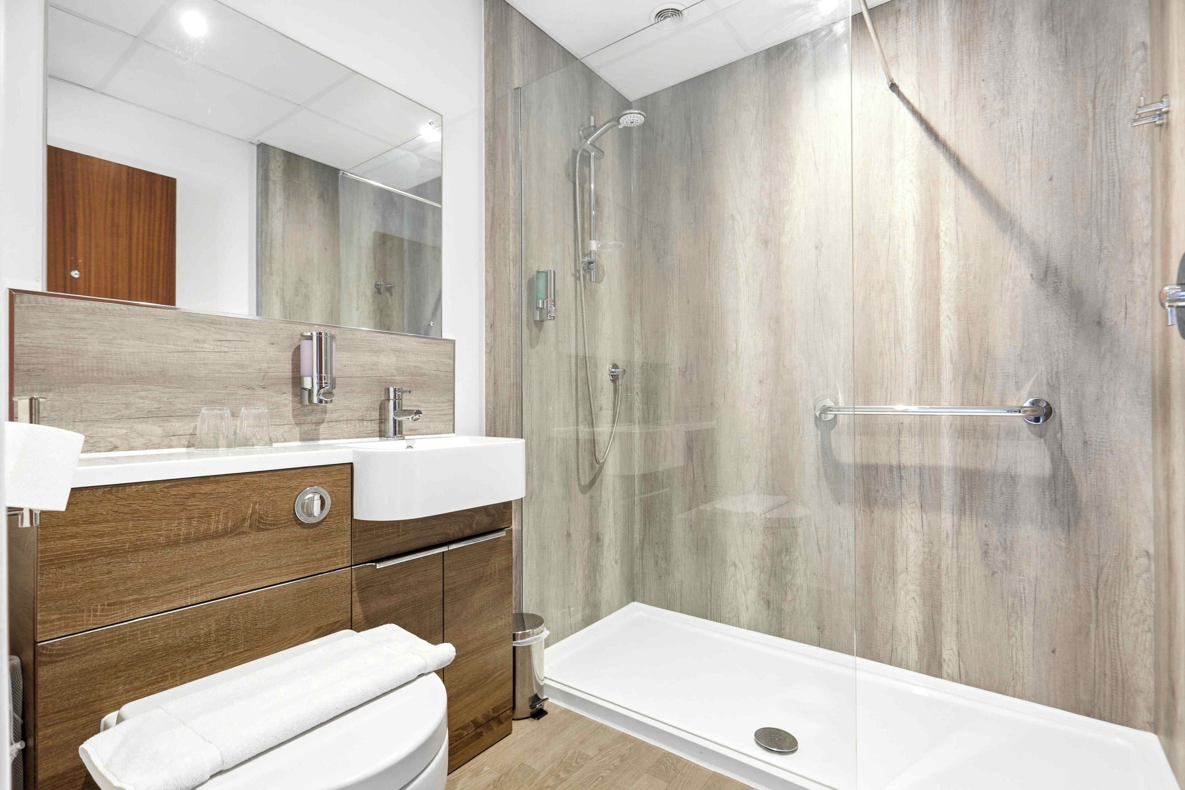A modern bathroom with a wooden vanity, a large mirror, a bathtub, and a shower enclosure.