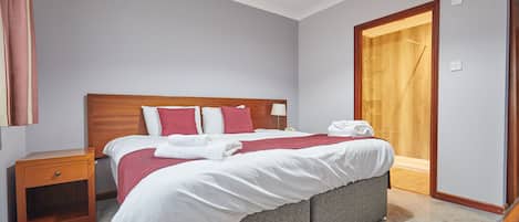 Una cama bien hecha con ropa de cama blanca y roja, un cabecero de madera y una mesita de noche con un cajón.