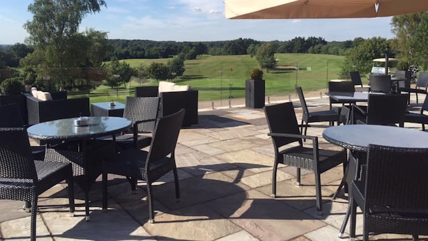 Une terrasse extérieure avec des tables et des chaises rondes, un grand parasol et une vue sur un terrain de golf.