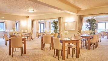 A spacious conference room with multiple tables and chairs, large windows, and a carpeted floor.