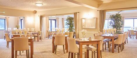 A spacious conference room with multiple tables and chairs, large windows, and a carpeted floor.