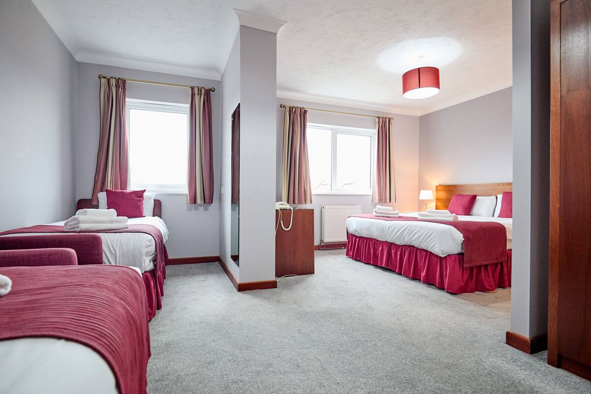Une chambre d’hôtel avec deux lits, une armoire en bois, un radiateur et une fenêtre avec des rideaux.