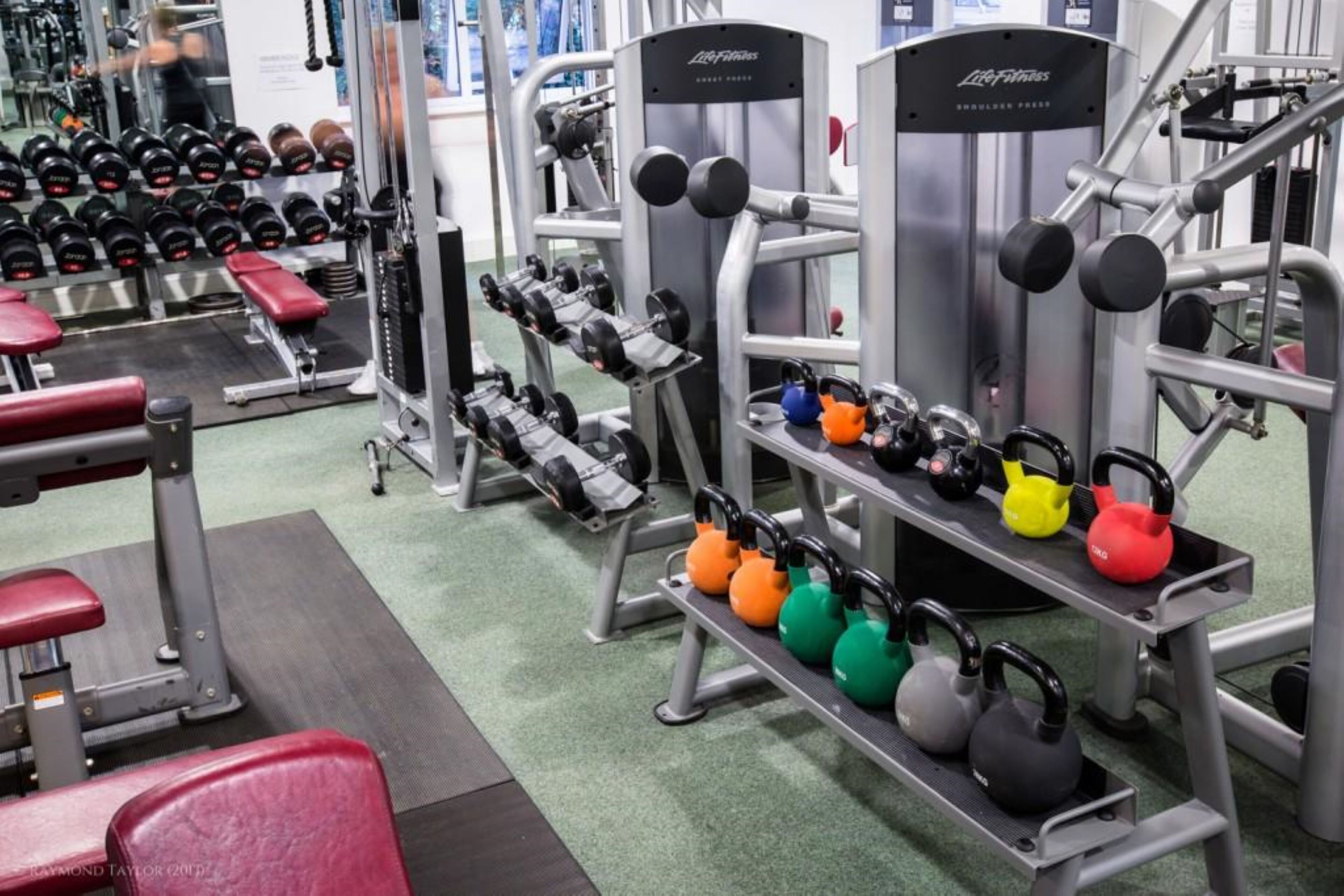A gym with weightlifting equipment, benches, and kettlebells.