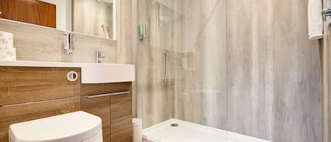 Un baño moderno con ducha acristalada, inodoro blanco y tocador de madera.