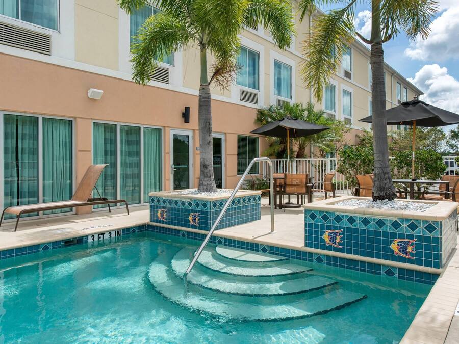 A swimming pool with steps leading into it, surrounded by palm trees and outdoor seating.