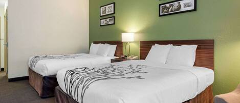 Una habitación de hotel con dos camas, una pared verde, cuadros enmarcados y una mesita de noche con una lámpara.