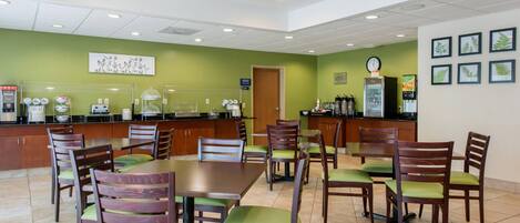 A dining area with wooden tables and chairs, a ceiling fan, and a kitchen area with appliances and a refrigerator.