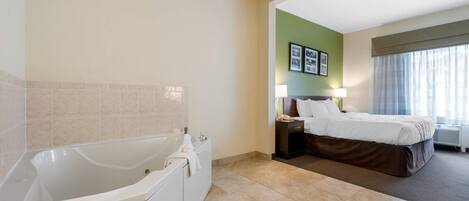 A hotel room with a large bathtub, a bed with a brown headboard, and a nightstand with a lamp.
