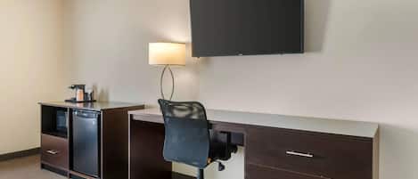 A hotel room with a desk, chair, TV, lamp, and a minibar.
