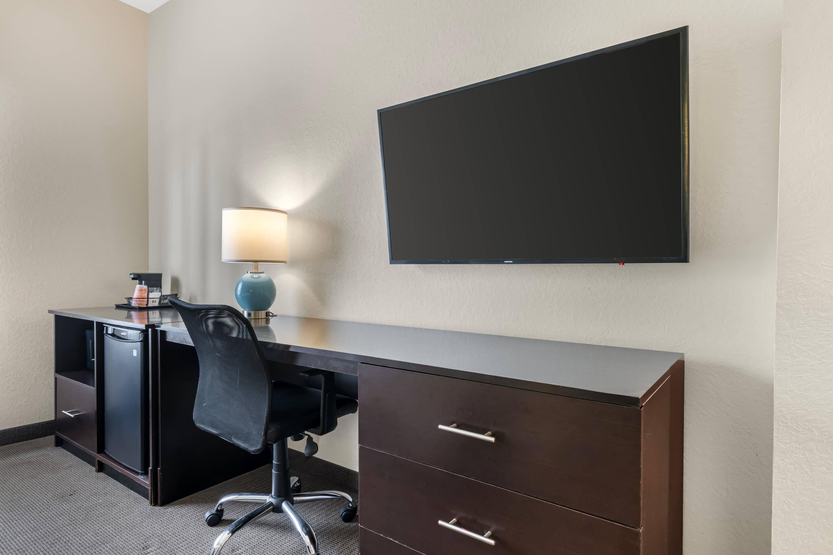 Une chambre d’hôtel équipée d’un bureau, d’une chaise, d’une lampe et d’un téléviseur à écran plat fixé au mur.