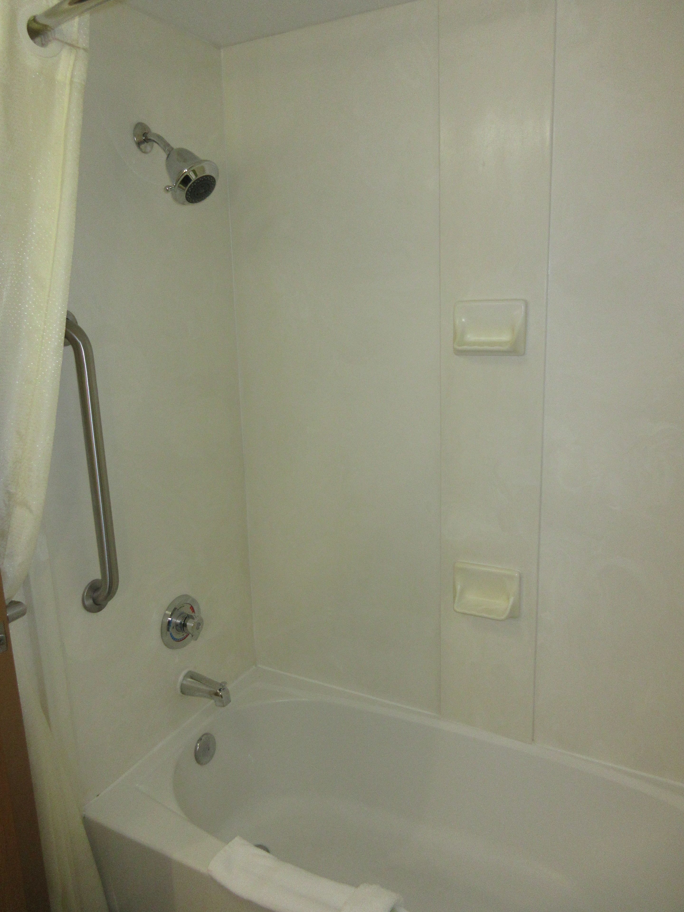A bathroom with a bathtub, a shower, and a handrail.
