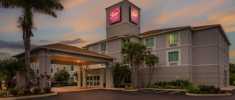 Un hotel con un llamativo letrero de Sleep Inn & Suites, una entrada techada y un camino de entrada arbolado.