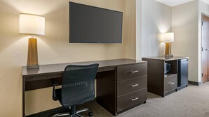 Une chambre d’hôtel avec un bureau en bois foncé, un fauteuil de bureau noir, un téléviseur à écran plat fixé au mur et une petite kitchenette équipée d’un four à micro-ondes et d’un réfrigérateur.