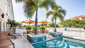 Un espace piscine aménagé avec des chaises longues, des parasols et des jardinières carrelées.