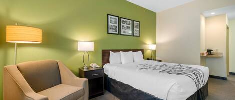 A hotel room with a bed, a chair, two bedside tables with lamps, and three framed pictures on the wall.