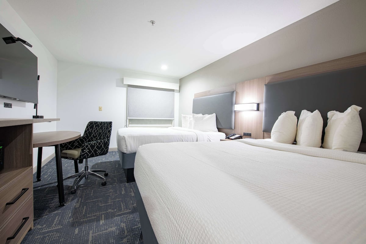 Habitación de hotel con dos camas, un escritorio, una silla, un televisor y una ventana.