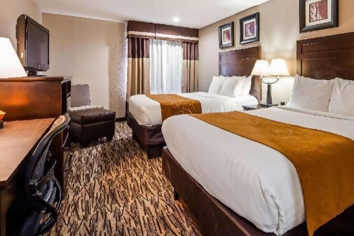A hotel room with two beds, a desk with a television, a chair, a lamp, and framed pictures on the wall.