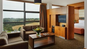 A modern hotel room with a large window, a sofa, a coffee table, a TV, and a wooden cabinet. - The Gateway Hotel (Dundalk)
