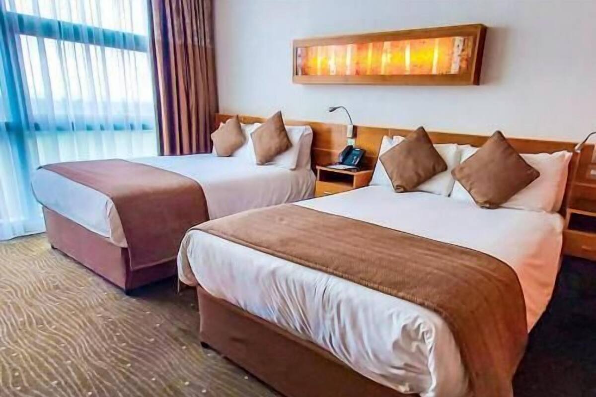 A hotel room with two beds, a nightstand, a lamp, and a painting on the wall.
