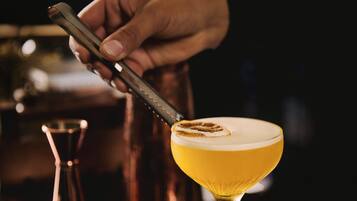 A hand using a tool to garnish a cocktail in a martini glass.