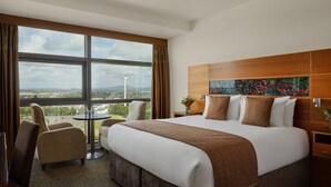 A hotel room with a large bed, a view of the cityscape, a round table, and a chair. - The Gateway Hotel (Dundalk)