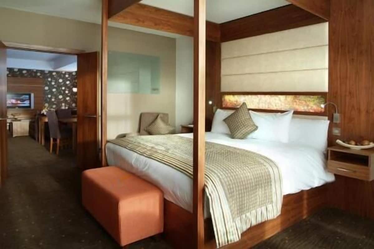 A hotel room with a bed, a wooden headboard, a bedside table, and a small seating area with a bench.