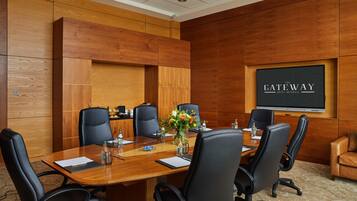 A conference room with a wooden panel wall, a large screen displaying "The Gateway Hotel Bunbury," and a table set for six with chairs.