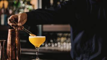 A bartender preparing a cocktail with a shaker and a martini glass on a bar counter.
