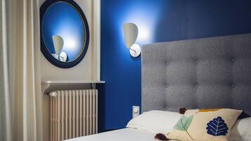 A bedroom with a tufted headboard, a round mirror, and a wall-mounted light fixture.